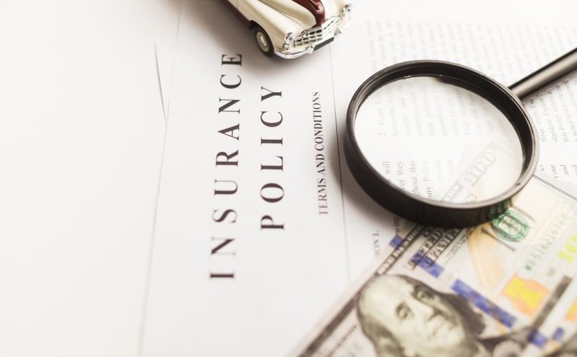 Auto insurance policy document reviewed with a magnifying glass beside cash and a toy car