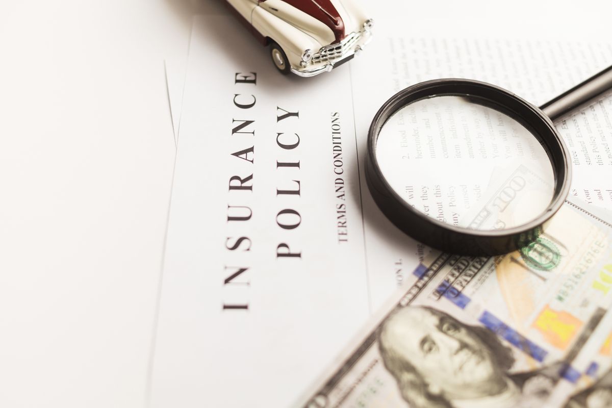 Auto insurance policy document reviewed with a magnifying glass beside cash and a toy car